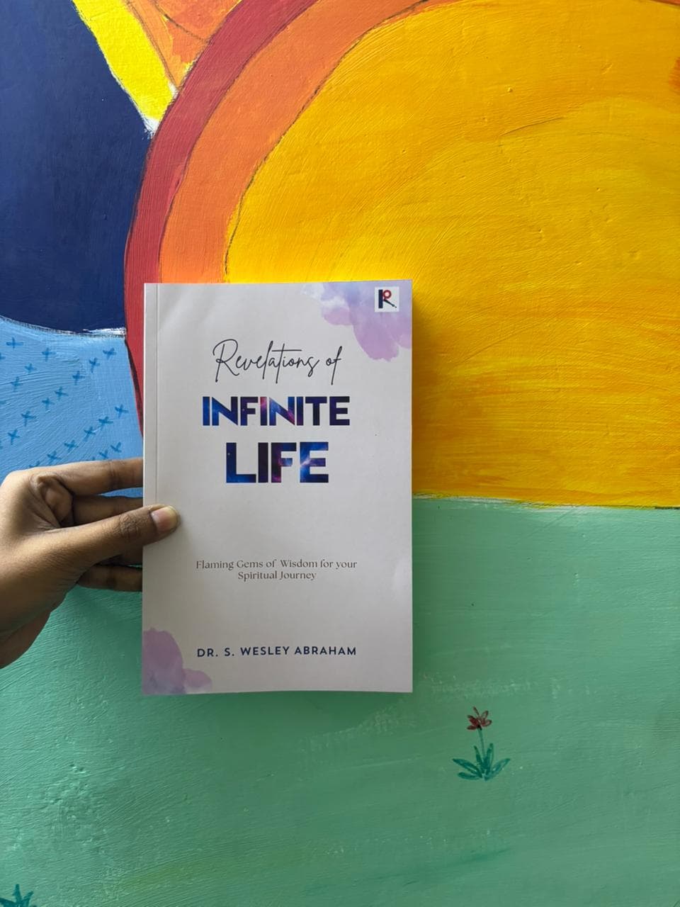 An author holding their finished copy of Revelations of Infinite Life, published by Ritera